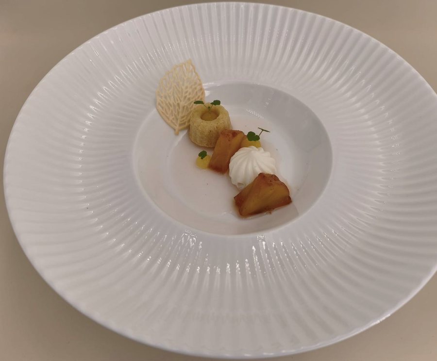 Dessert auf weißem Rillenteller: kleines Küchlein, karamellisierte Ananas, Sahnetuff und filigrane Tuile