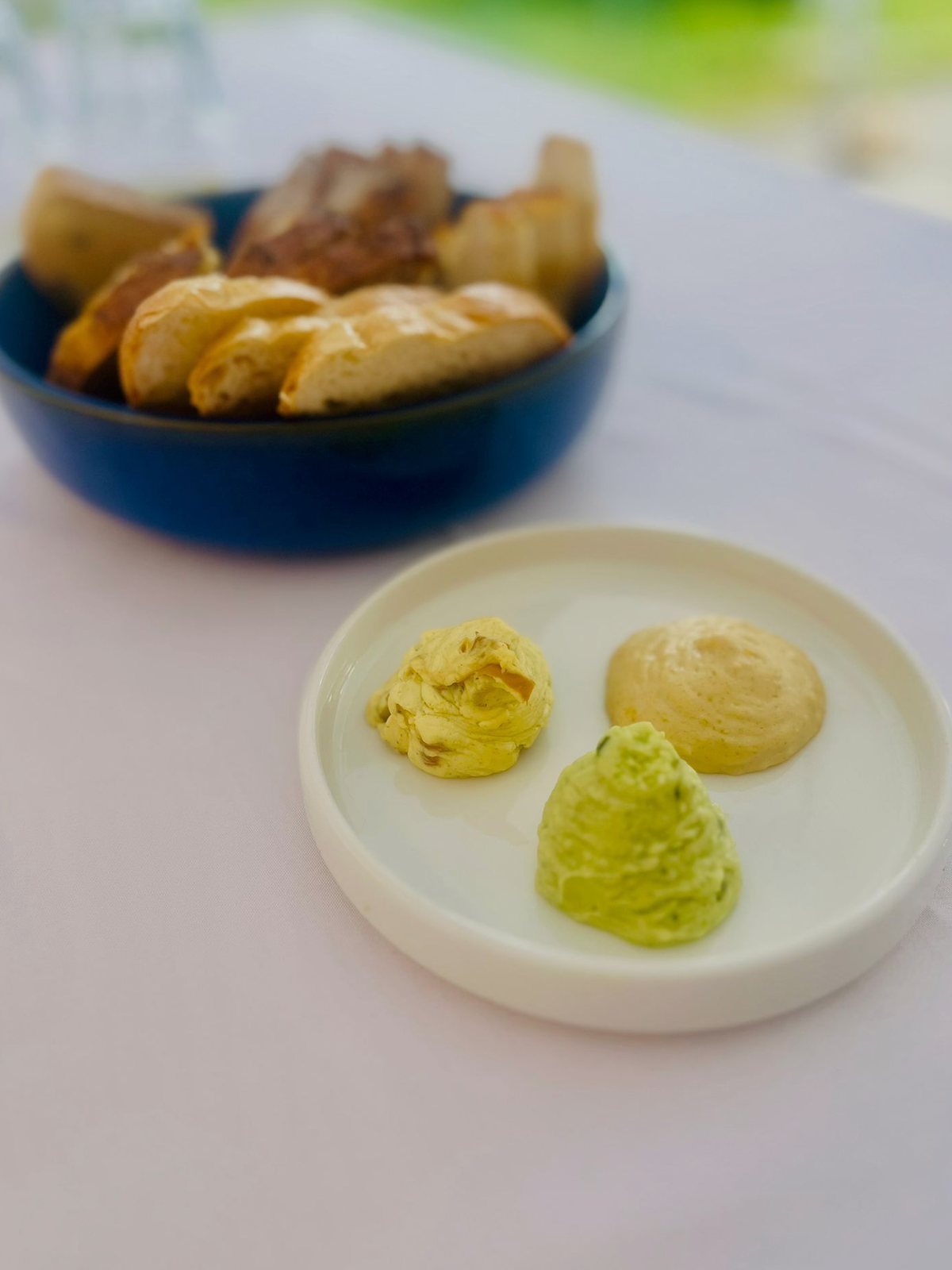 Brotkorb in blauer Schale, davor ein weißes Tellerchen mit drei hausgemachten Buttervariationen