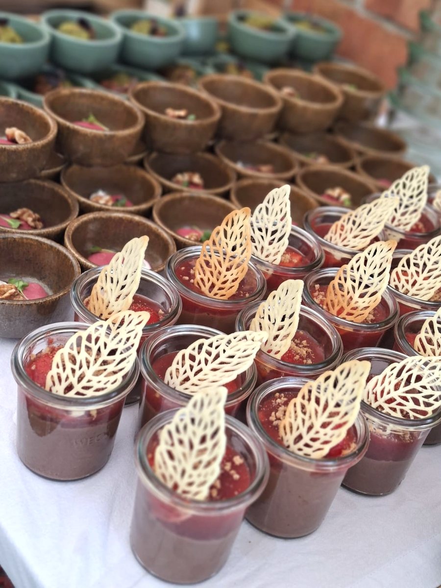Buffet-Aufbau im Freien: Gläser mit Schokoladencreme, Fruchtspiegel und Tuile-Blatt, dahinter Reihen brauner und grüner Schälchen