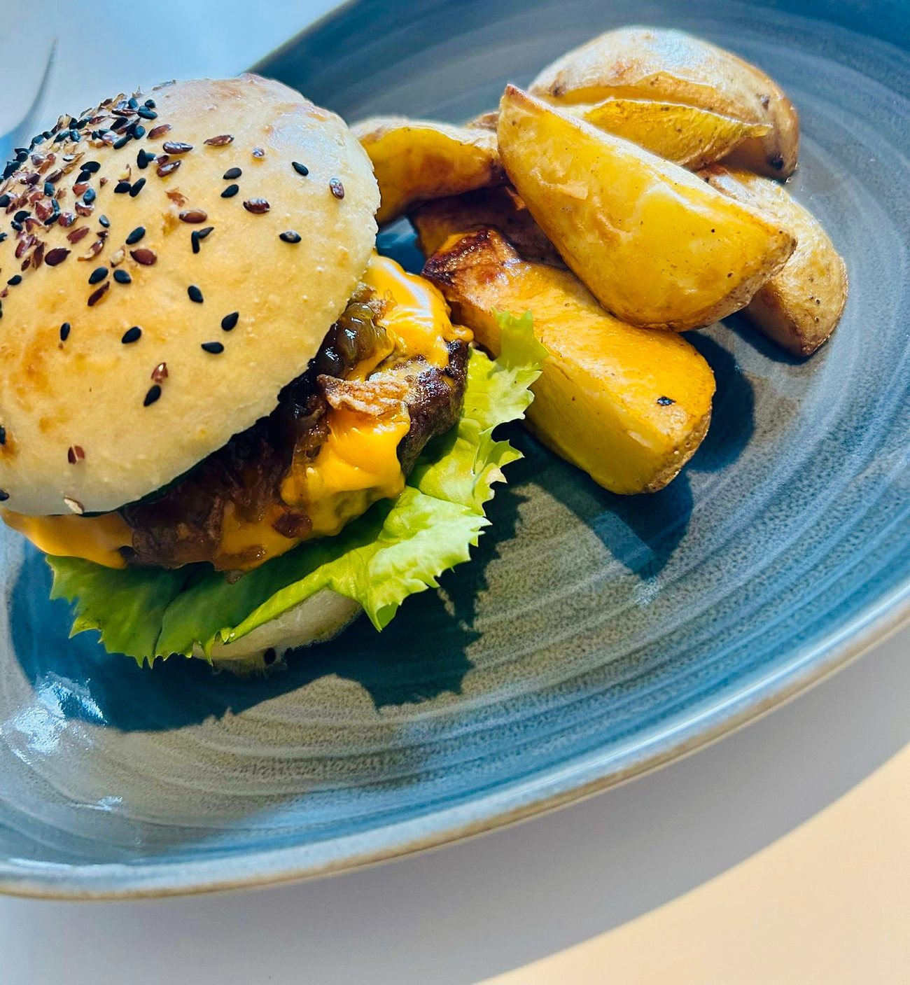 Burger mit Cheddar, Salat und Kartoffelspalten auf blaugrauem Teller