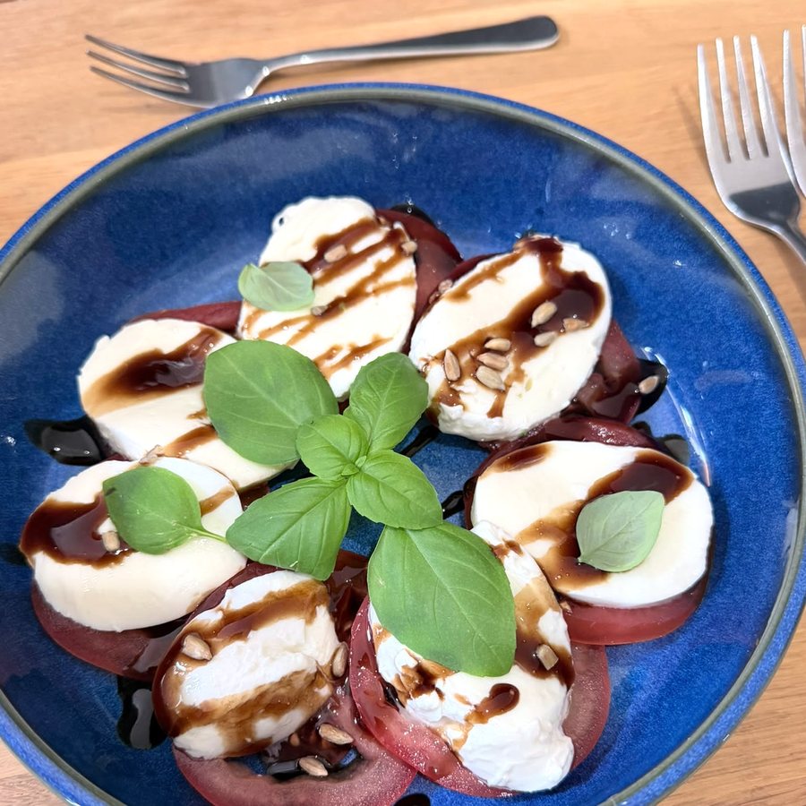 Caprese aus Mozzarella, Tomate, Pinienkernen und Balsamico-Reduktion mit Basilikum auf tiefblauem Teller