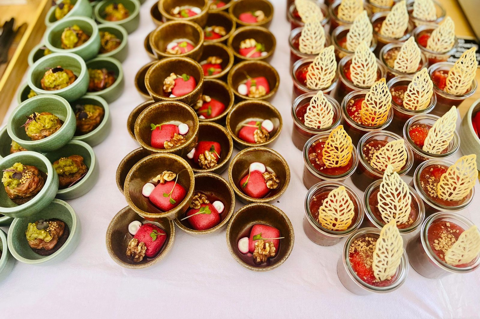 Fingerfood-Buffet von oben: Reihen grüner Schälchen, brauner Schälchen mit Rote-Bete-Würfeln und Walnuss sowie Gläser mit Fruchtspiegel und filigranen Tuile-Blättern