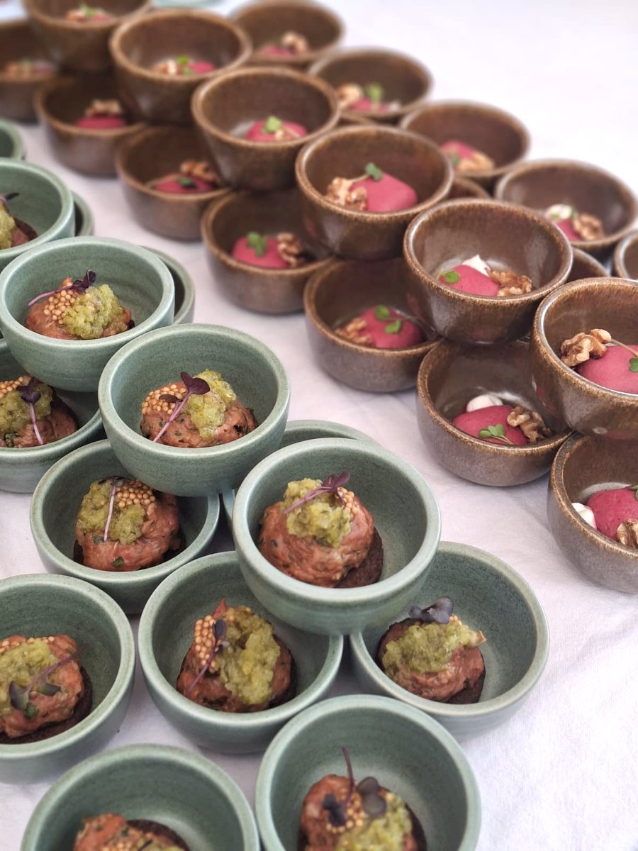 Grüne Schälchen mit Tatar und Kräuterkruste vor braunen Schälchen mit Rote-Bete-Creme auf weißer Tischdecke