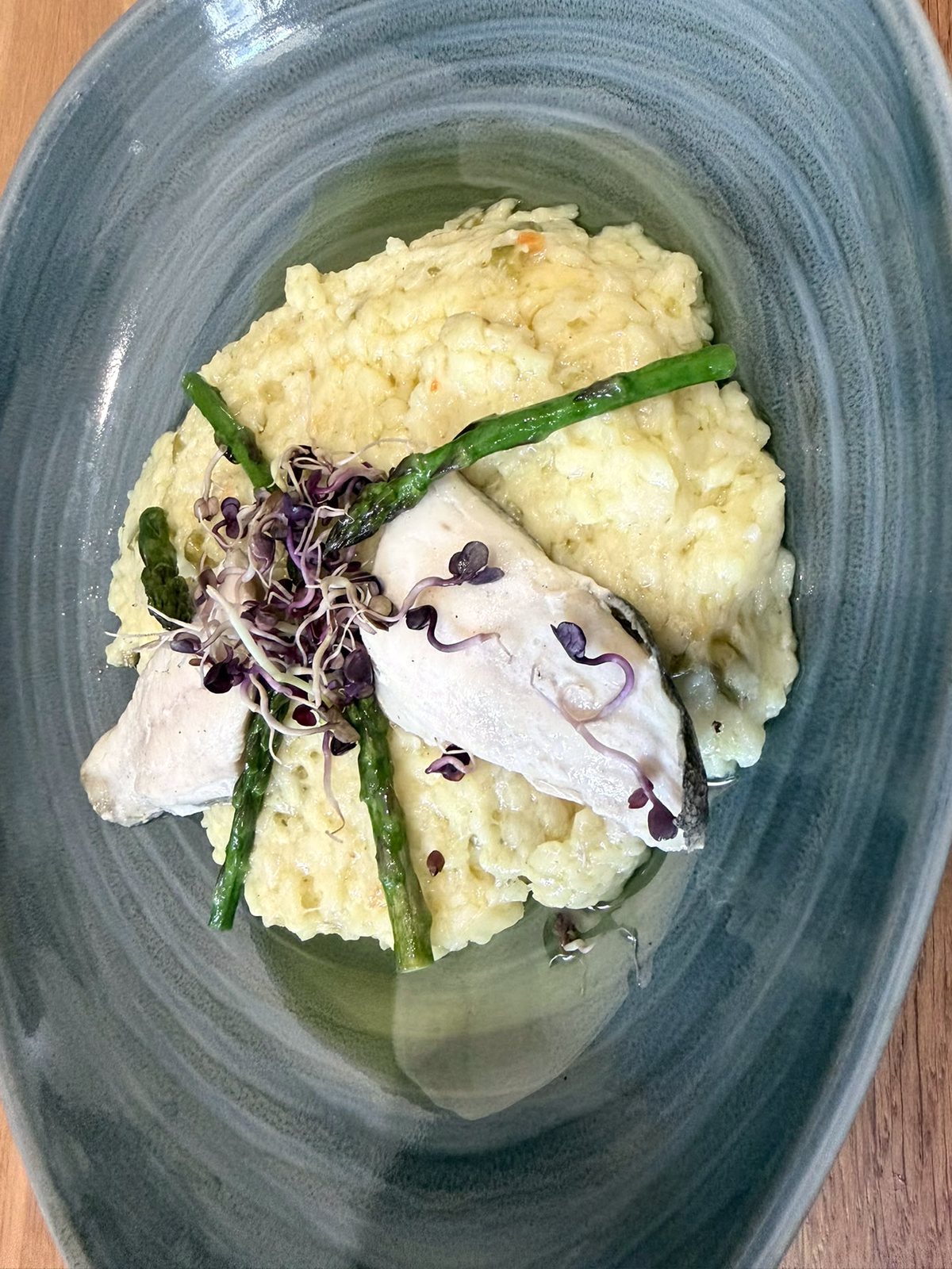 Zartes Fischfilet auf Risotto mit grünem Spargel und roter Kresse in blaugrauer Schale