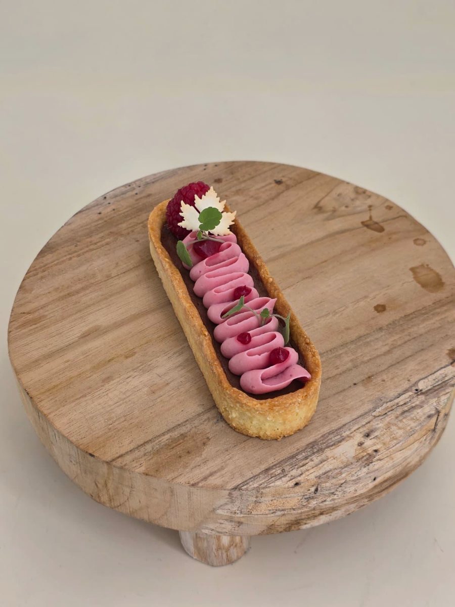 Längliche Himbeer-Tarte mit Cremetuff-Reihe und essbarer Blüte auf einer Holzscheibe