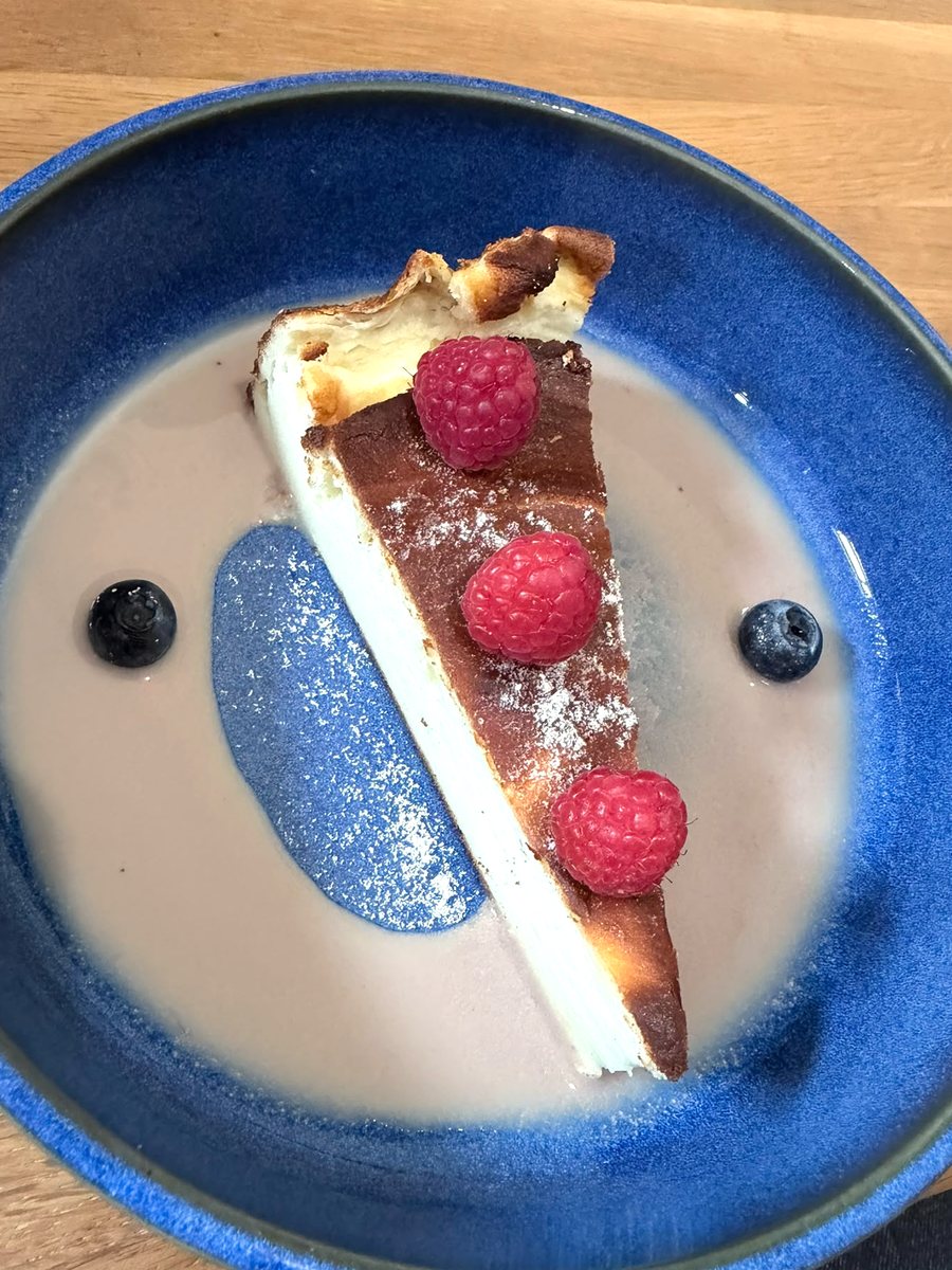 Käsekuchen-Stück mit Himbeeren, Heidelbeeren und Fruchtsauce auf tiefblauem Teller