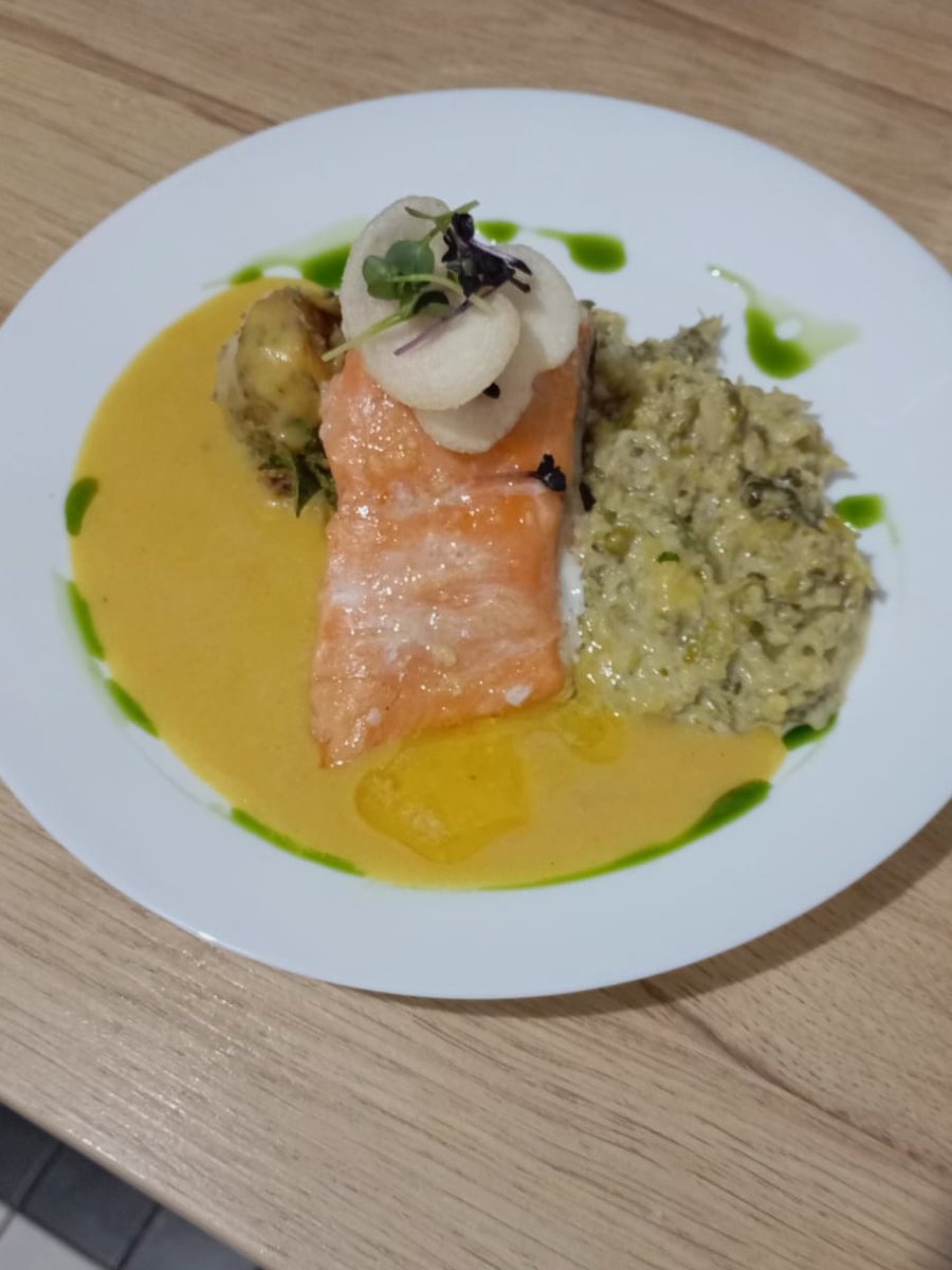 Lachsfilet mit Safransauce, Kräuteröl und Risotto auf weißem Teller, garniert mit hellen Gemüsescheiben und Kresse