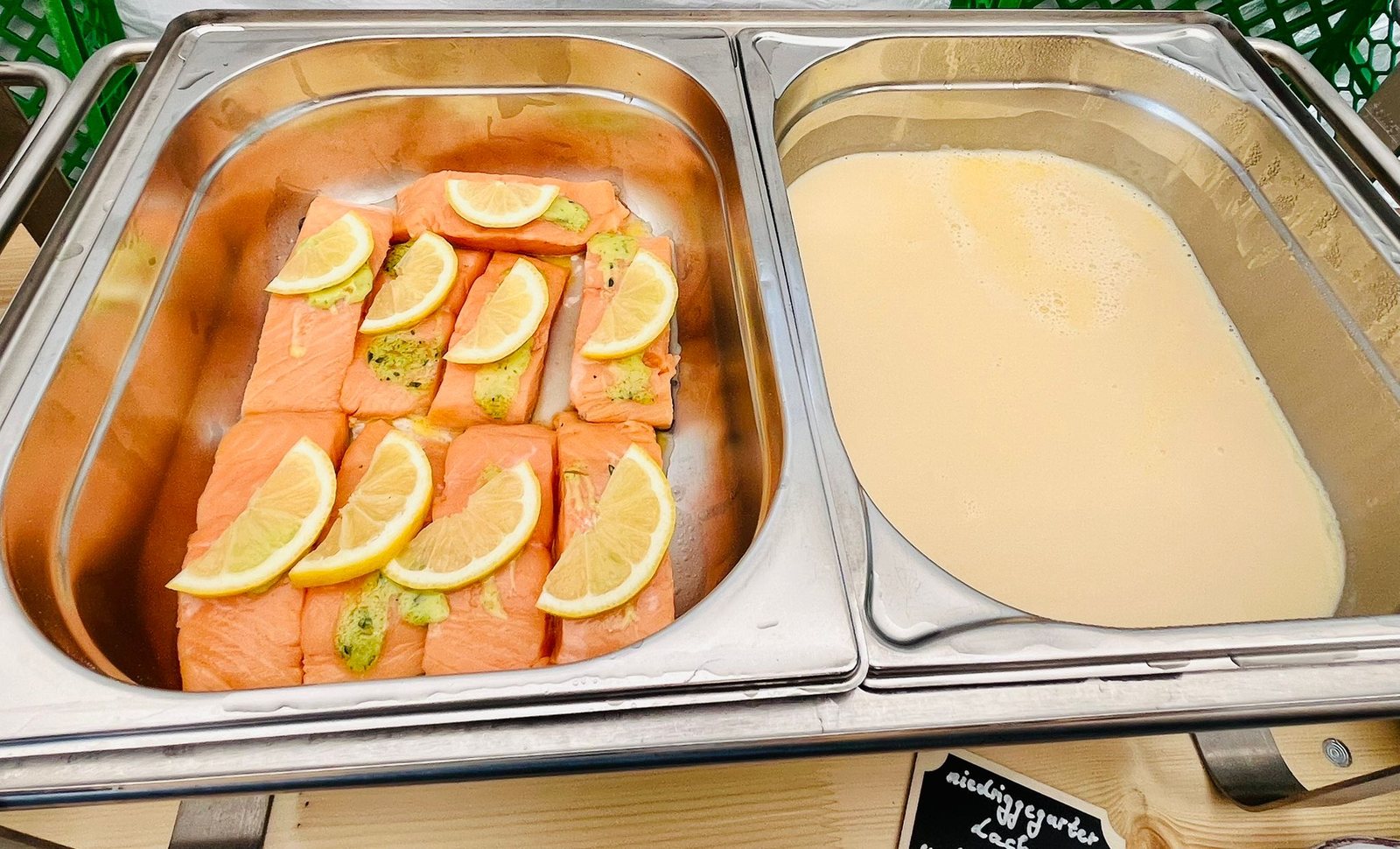 Lachsfilets mit Zitronenscheiben in einem Gastronorm-Behälter, daneben eine helle Sauce