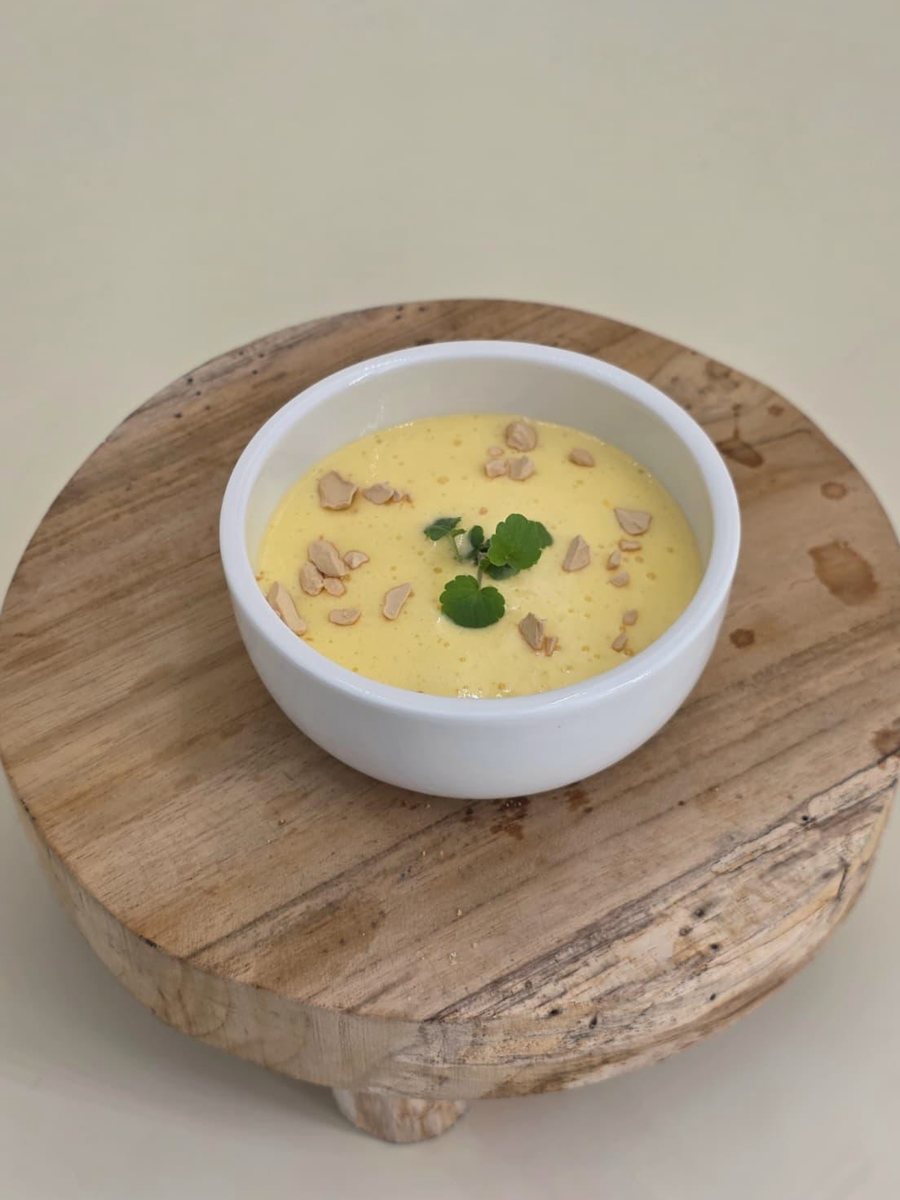 Mango-Safran-Creme mit Nusskrokant und Kresse in weißer Schale auf einer Holzscheibe