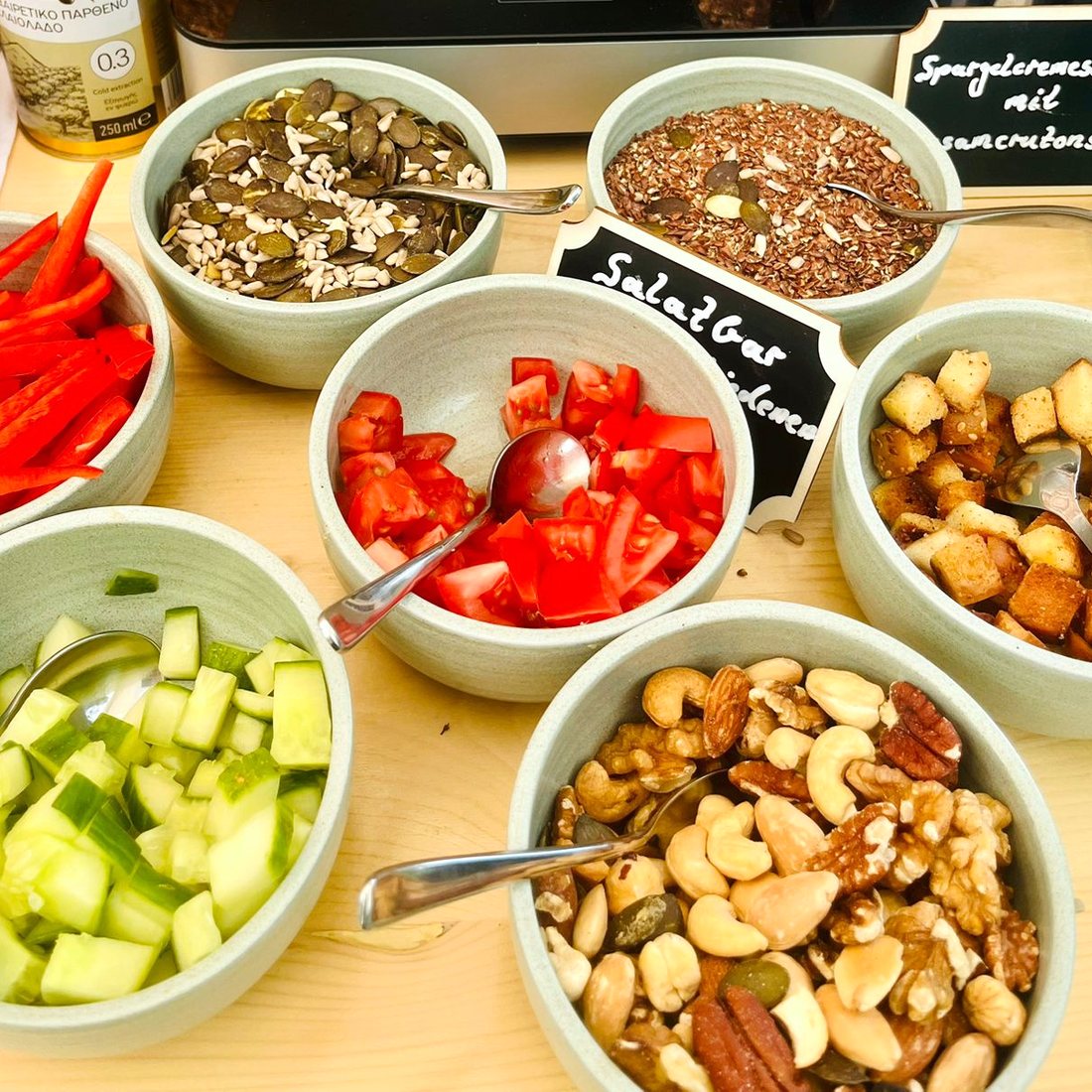 Salatbar-Aufbau: Schälchen mit Gurke, Paprikastreifen, Tomate, Nüssen, Croutons und Kernen, dazu handbeschriebene Kreidetafeln