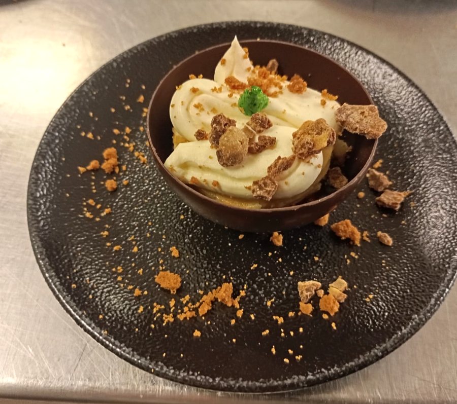 Schokoladen-Halbkugel mit Cremetuff und Nusskrokant auf schwarzem Teller