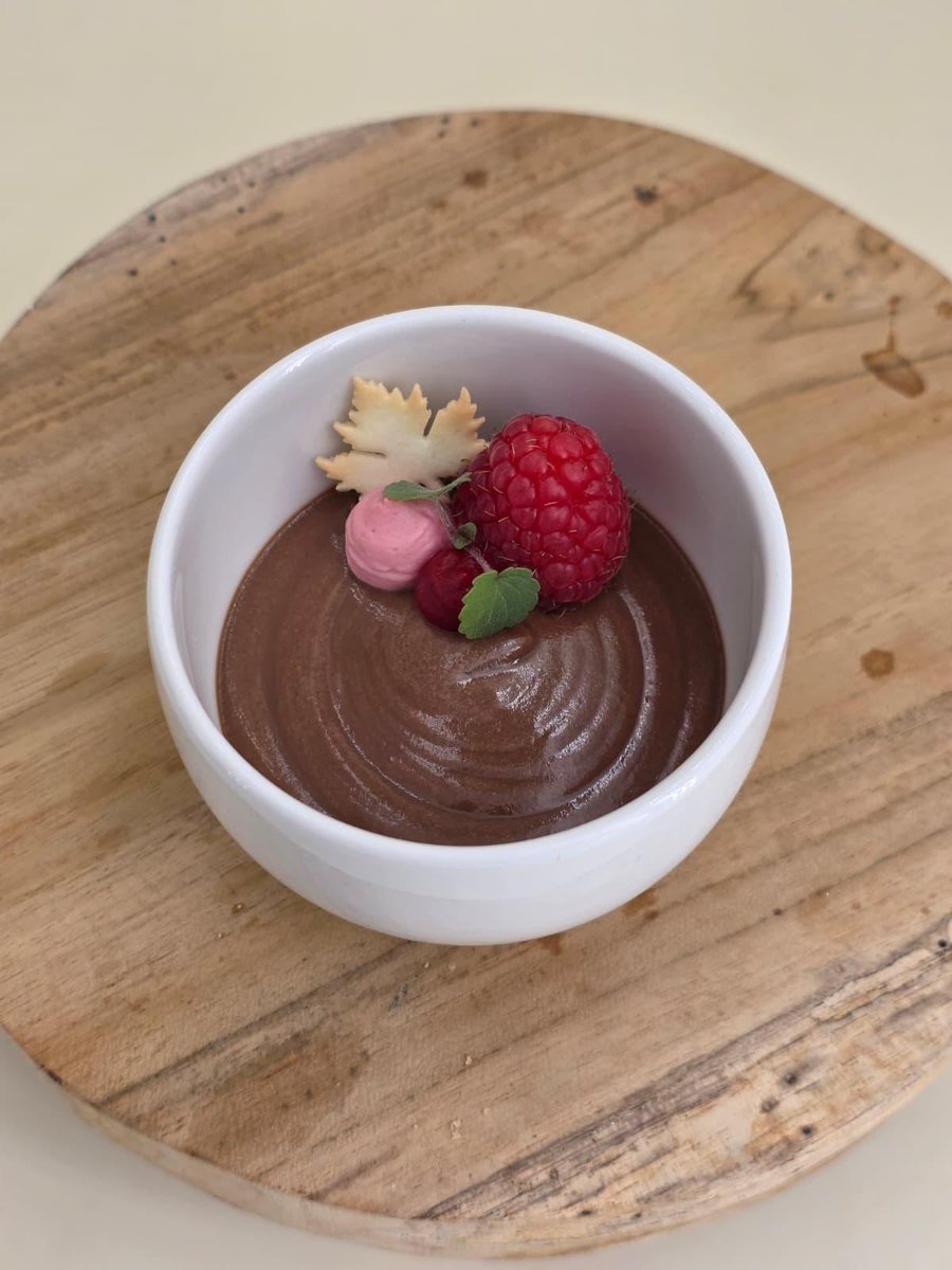 Schokoladenmousse in weißer Schale mit Himbeere, Schokoblatt und Minze auf einer Holzscheibe